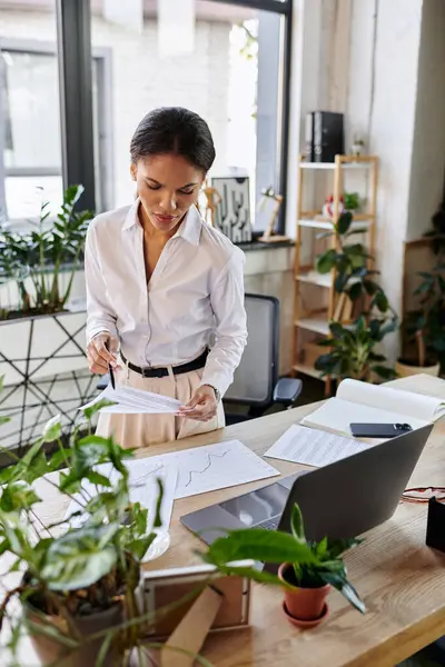 A young Black businesswoman reviews reports in her stylish, plant-filled office. — Stock Photo