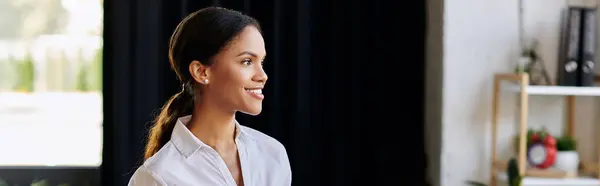 A professional woman in a white shirt smiles while working in a sleek office space, banner — Stock Photo