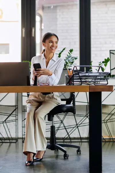 A young african american businesswoman engages with her phone in a bright modern workspace. — Stock Photo