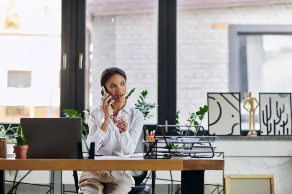 A young African American woman handles calls and manages tasks in a contemporary workspace. — Photo de stock