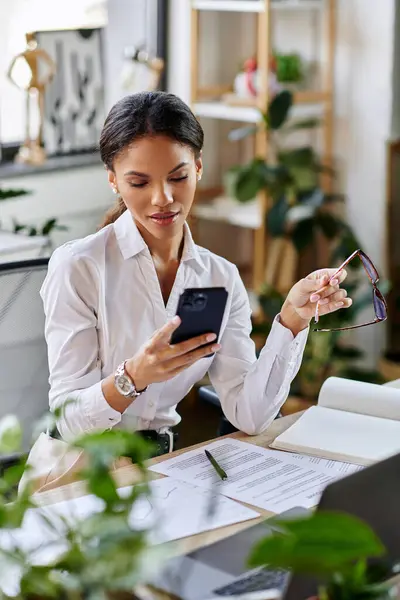 A young African American businesswoman in a white shirt focuses on her smartphone while at work. — Stock Photo
