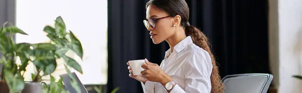 Young African American businesswoman in a white shirt sips coffee while focused on her laptop, banner — Stock Photo