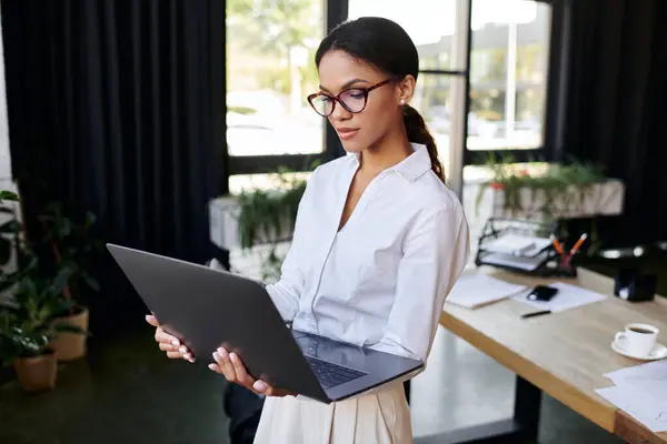 Young businesswoman in a white shirt engages with her laptop in a modern workspace. — Stock Photo