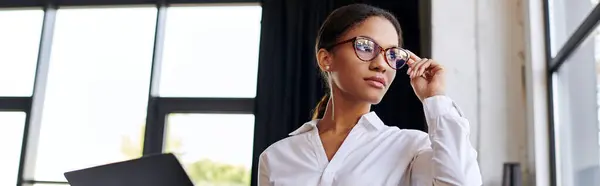 A young Black businesswoman in a white shirt reviews her work in a modern office, banner — Stock Photo