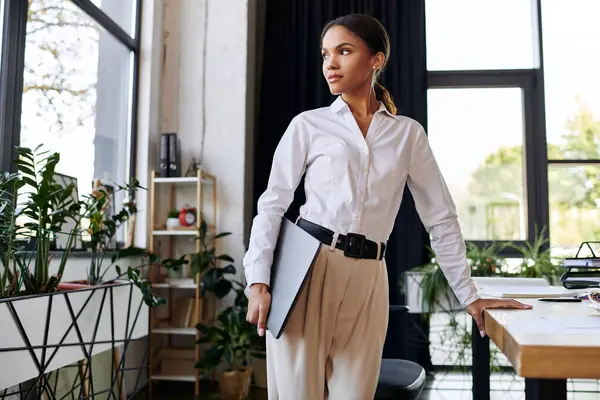 A young African American woman in a white shirt confidently engages in her work amidst greenery. — Stock Photo