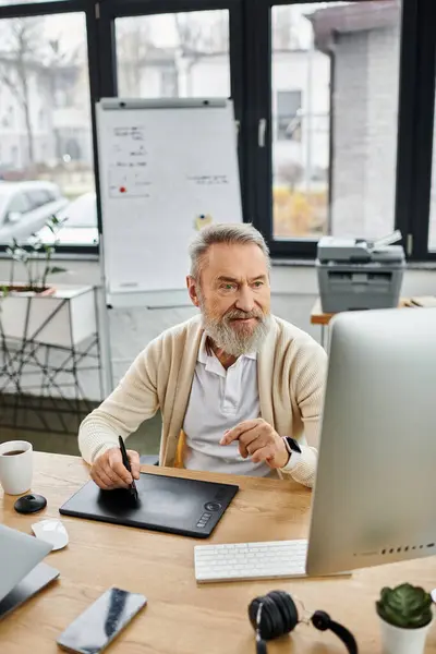 A mature man focuses on digital art in his office, surrounded by plants and a graphics tablet. — Stock Photo