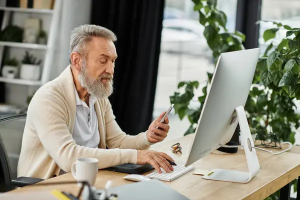 Un uomo bello maturo si concentra sui suoi compiti su una scrivania moderna, controllando il suo telefono in luce naturale. — Foto stock
