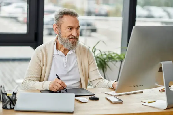 Homme âgé avec une barbe s'engage dans le travail numérique à un bureau spacieux avec plantes. — Photo de stock