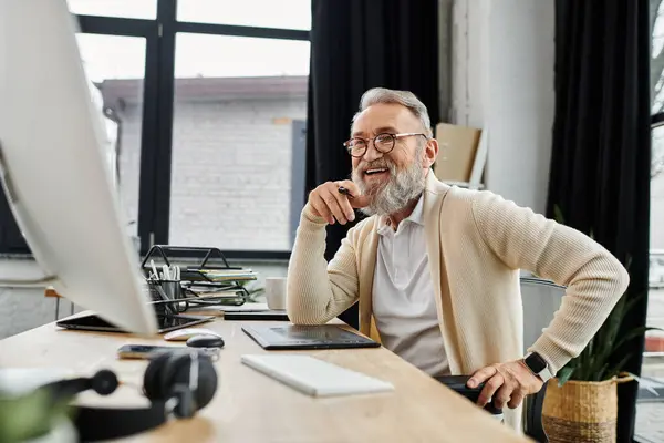 Handsome senior man smiles while working at his desk during the afternoon light. — Stock Photo