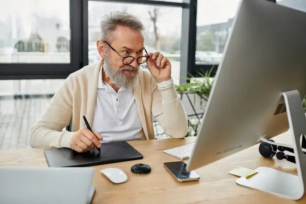 A mature handsome man is focused on his tasks at a sleek workspace with natural light. — Stock Photo