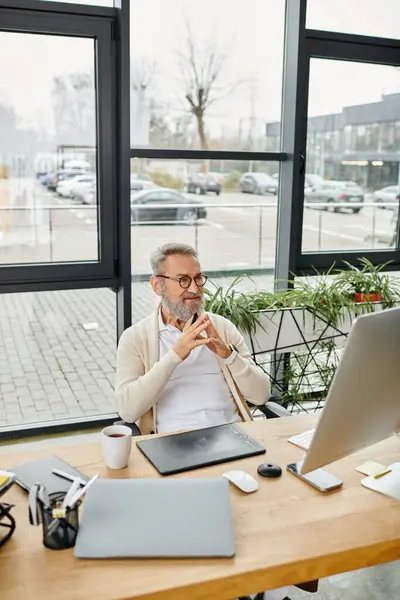 Bello uomo anziano si impegna in un profondo pensiero mentre lavora alla sua scrivania in un ufficio contemporaneo. — Foto stock