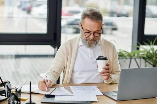 Skilled man reviews documents while enjoying coffee at a stylish workspace with natural light. — Stock Photo