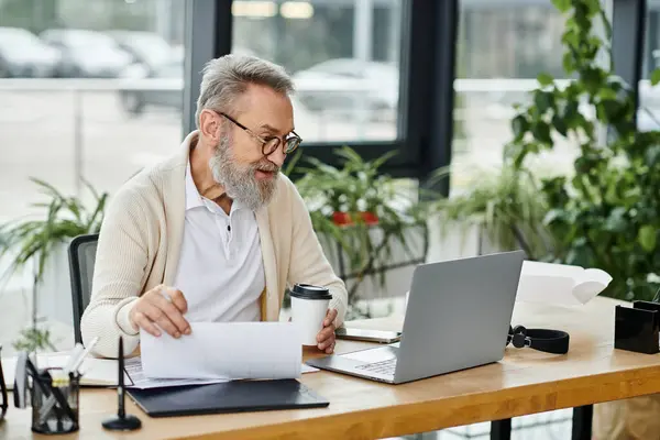 A mature handsome man with a beard is focused on reviewing documents while seated at a desk. — Stock Photo