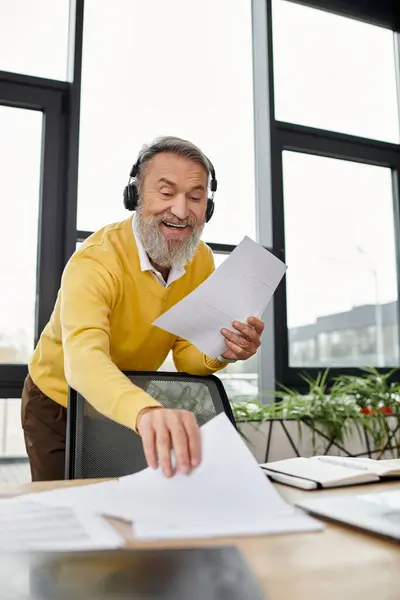 Senior man engages with papers at his desk, displaying joy and concentration in an office. — Stock Photo