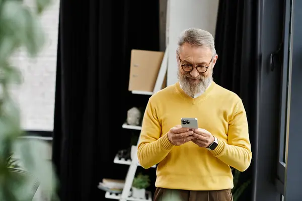 Man enjoys browsing on his smartphone while standing in a warm, inviting room. — Stock Photo