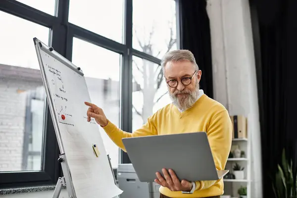 Handsome senior man shares insights while using a laptop in a well lit office setting. — Stock Photo