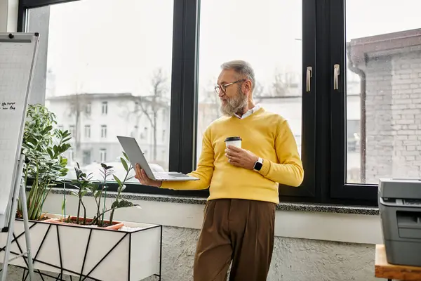 Schöner älterer Herr greift entspannt mit einer Kaffeetasse in der Hand zu seinem Laptop — Stockfoto