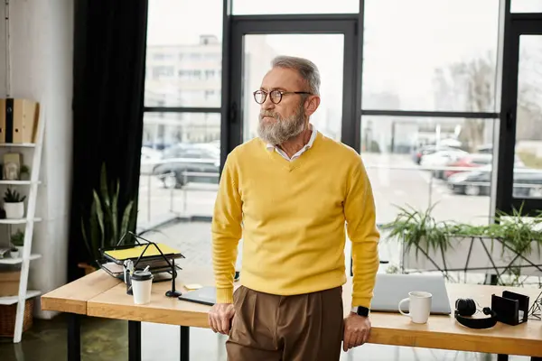 Ein reifer, gutaussehender Mann mit gelbem Pullover und Brille beobachtet sein Büroumfeld. — Stockfoto