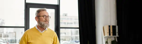 Красивий зрілий чоловік з бородою стоїть в стильному приміщенні, наповненому світлом. — стокове фото