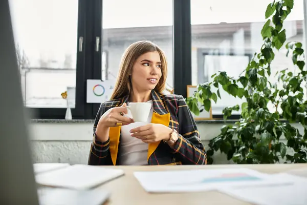 Young woman in a checkered blazer relaxes with coffee during a productive workday in the office. — Stock Photo