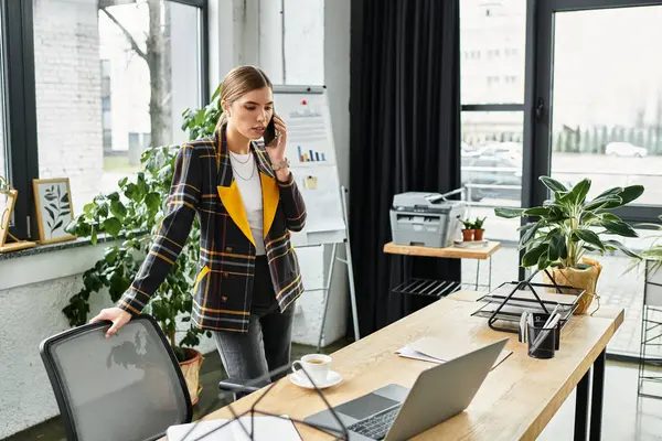 Una giovane donna in un blazer a scacchi chic è in rete durante la gestione di compiti nel suo ufficio. — Foto stock