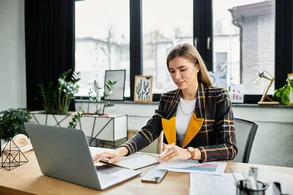 Jeune femme élégante analyse les rapports à son bureau avec un ordinateur portable dans un bureau chic. — Photo de stock