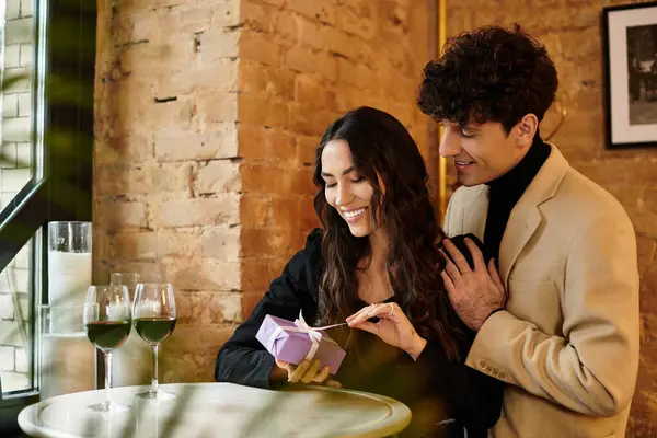 Young couple enjoys a special moment together while unwrapping a gift at a charming restaurant. — Stock Photo