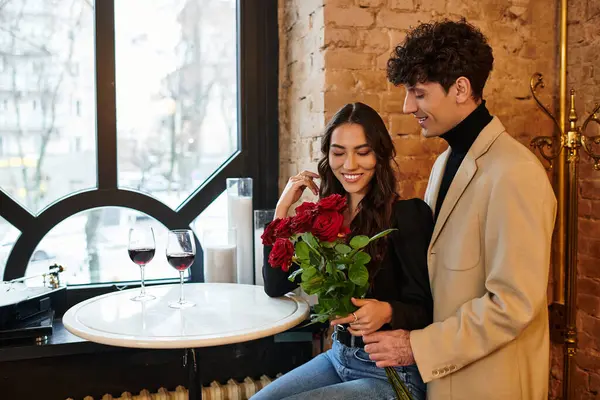 A young couple shares a romantic moment in a cozy restaurant, enjoying wine and flowers. — Stock Photo