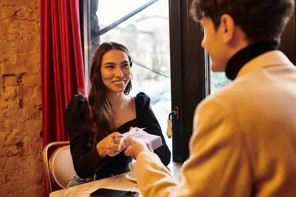 A couple exchanges thoughtful gifts, sharing smiles and love in a charming restaurant setting. — Stock Photo