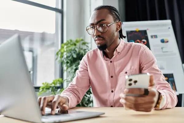 Young man collaborates on a project with a laptop and smartphone in a vibrant workspace setting. — Stock Photo