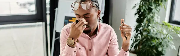 A young african american man sits thoughtfully in a bright, modern workspace, considering his next move. — Stock Photo