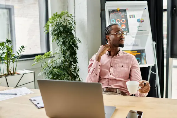 A young african american man sips coffee while working at a chic desk in a bright space. — Stock Photo