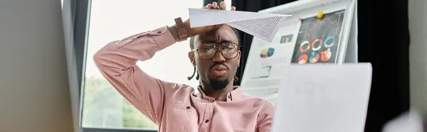 Young African American man struggles with focus while working remotely in a stylish workspace. — Stock Photo