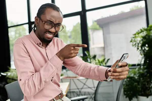 A young african american man interacts passionately with his smartphone in a modern workspace. — Stock Photo