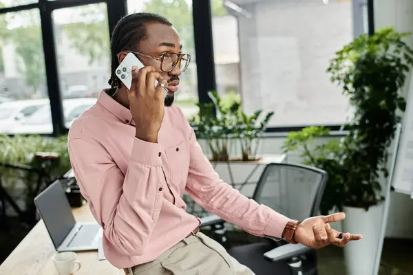 Joven se vincula con los clientes en su teléfono en un vibrante espacio de coworking, encarnando la vida nómada moderna. - foto de stock