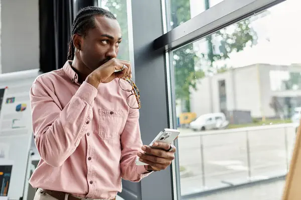 Young man using a smartphone, pondering ideas in a stylish, nomadic workspace. — Stock Photo