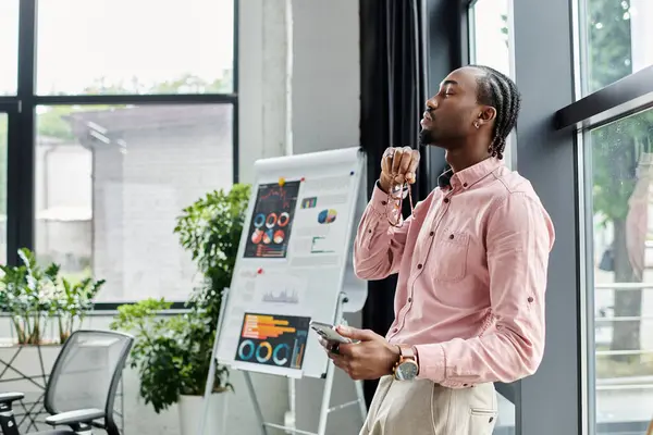 A young African American man ponders his next project in a vibrant workspace surrounded by plants. — Stock Photo