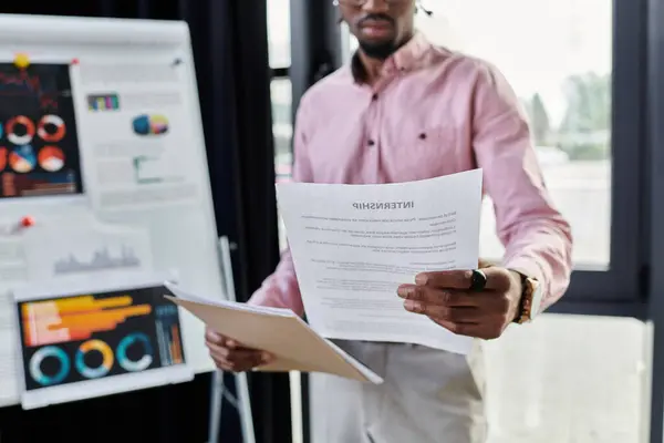 Un giovane uomo afroamericano si concentra sulle scartoffie in un ufficio moderno, incarnando la vita lavorativa a distanza.. — Foto stock