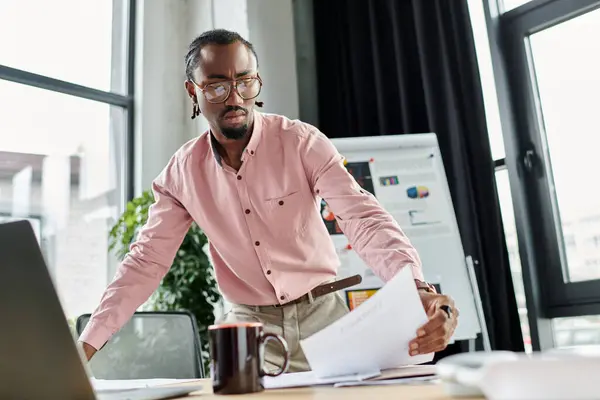 A young african american man reviews important documents while working remotely in a stylish office. — Stock Photo