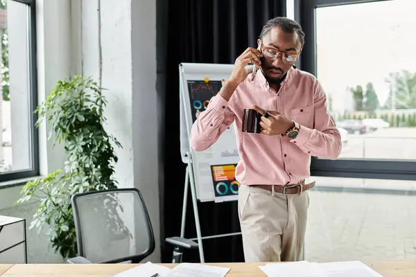 A young man dressed in business casual attire multitasks on a call while managing his workspace — Stock Photo