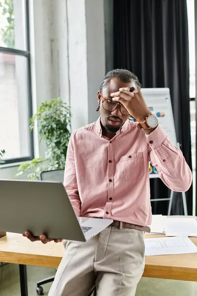 A young african american man looks stressed while working remotely in a contemporary office space. — Stock Photo