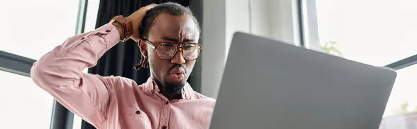 A young african american man concentrates on his laptop screen, revealing surprise and concern. — Stock Photo
