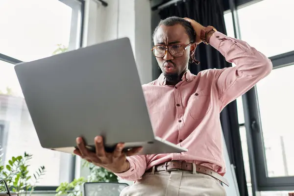 A young african american man looks surprised while focusing on his laptop in a stylish workspace. — Stock Photo
