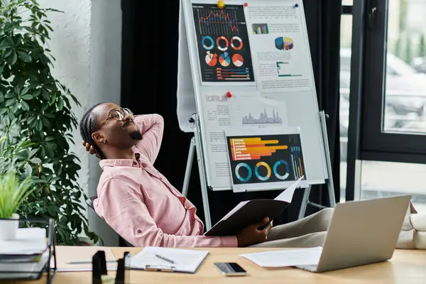 A young African American man relaxes while reviewing charts and data in a stylish workspace. — Stock Photo