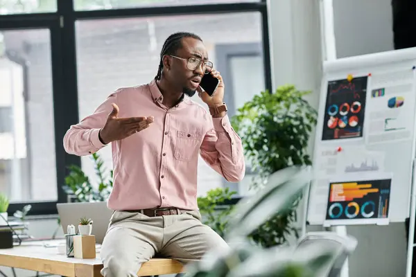 A handsome young digital nomad talks animatedly on his phone, surrounded by leafy plants. — Stock Photo