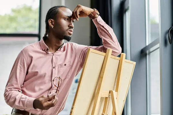 Ein junger afrikanisch-amerikanischer Mann denkt über seinen nächsten Schritt nach, während er Kunst in einem modernen Arbeitsraum schafft. — Stockfoto