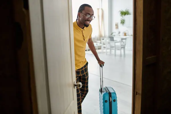 Ein stilvoller junger Mann betritt ein helles, einladendes Zimmer mit einem Koffer, bereit für Abenteuer. — Stockfoto