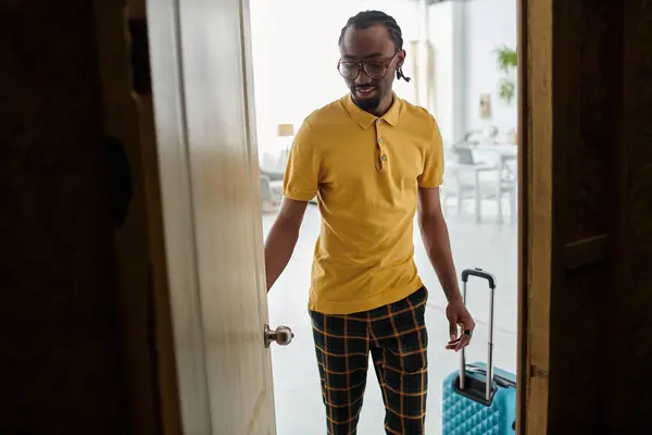 A young african american man enters a stylish space with a suitcase, ready for his remote work adventure. — Stock Photo