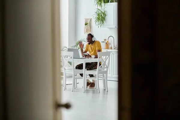Brightly lit kitchen with a young african american man engaged in remote work, showcasing nomadism. — Stock Photo