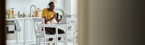 A young african american man is engaged in remote work while sitting at a modern kitchen table. — Stock Photo
